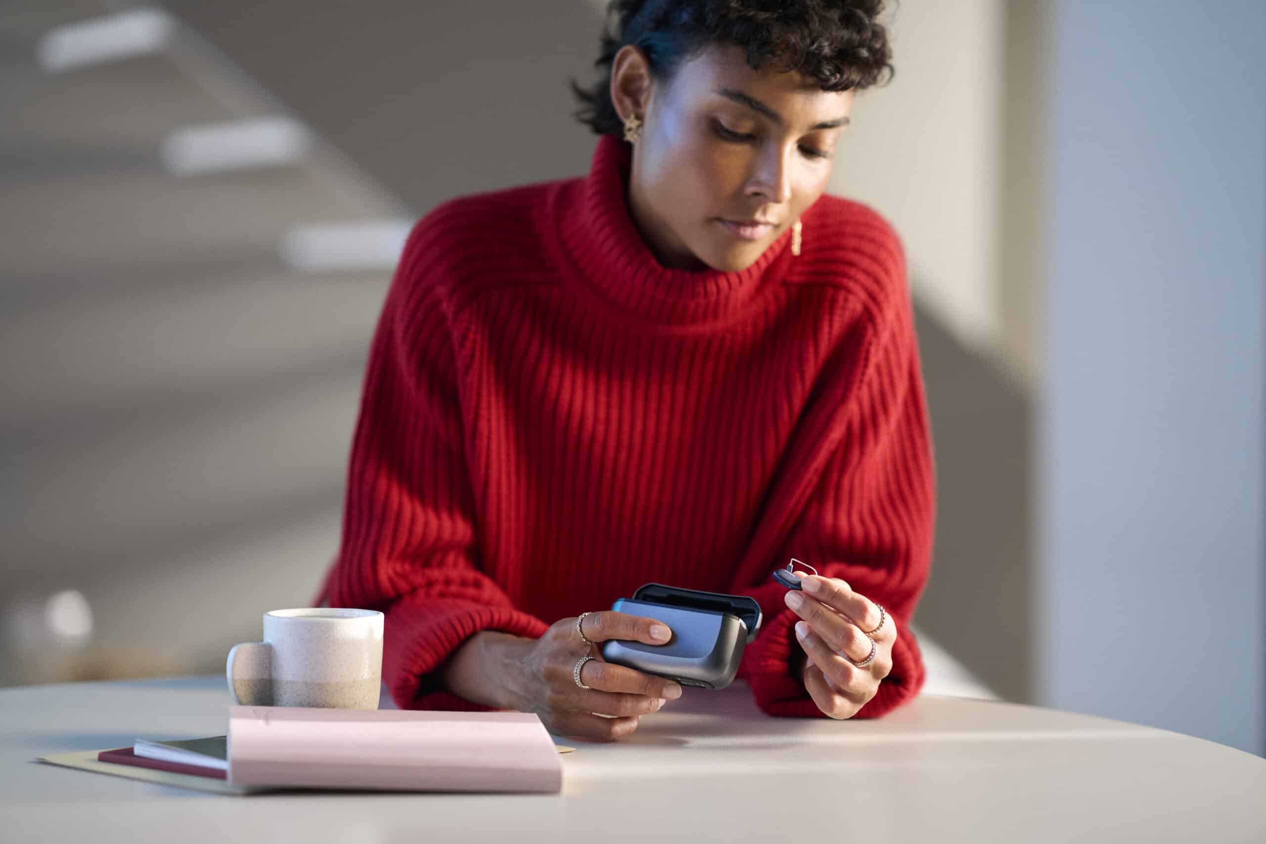 Person holding a hearing aid and a charger for the hearing aid